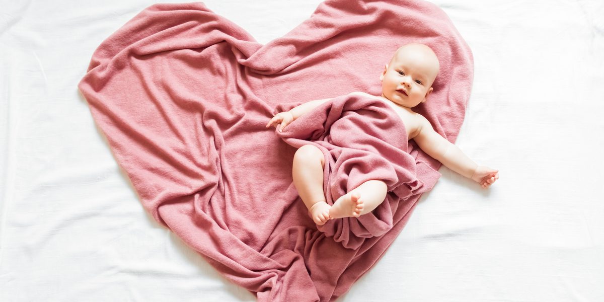 A baby lying on a pink blanket arranged in the shape of a heart