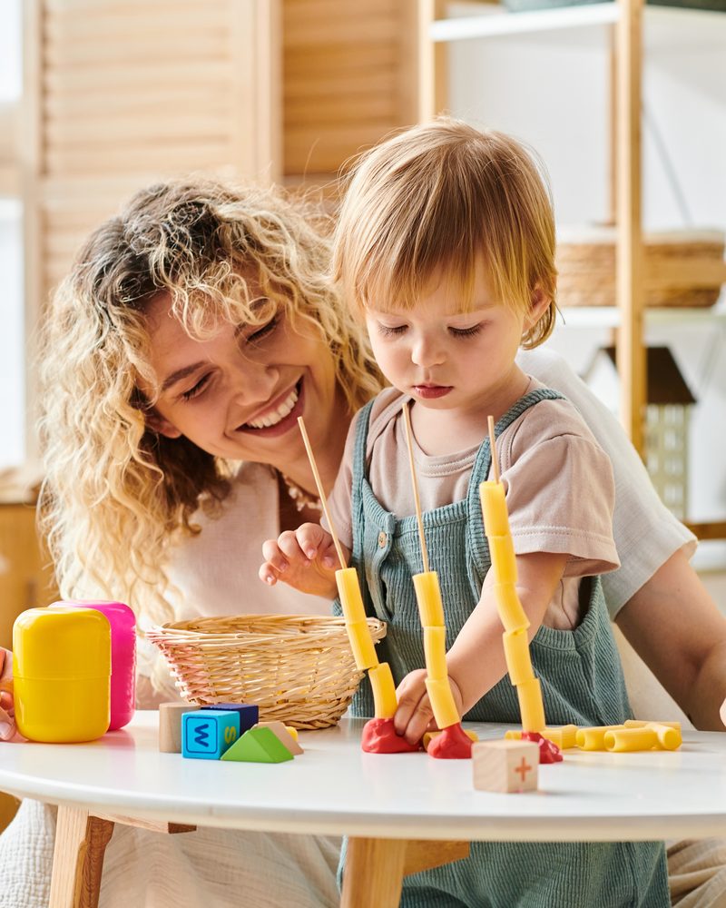 A mother and her toddler playing with a threading toy at a small table at home