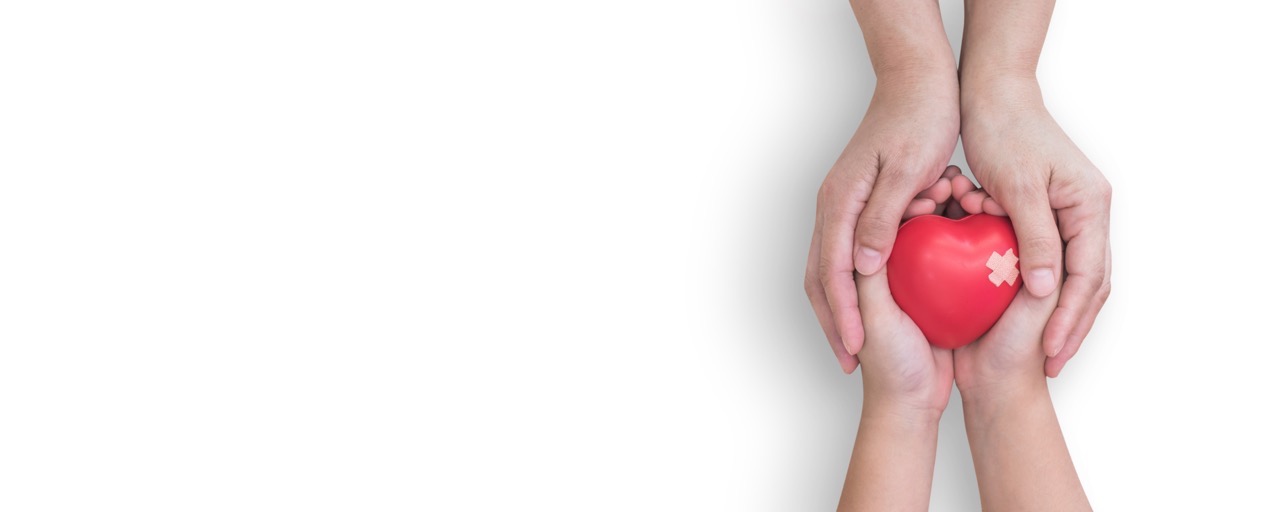 An adult's hands and a child's hands cupped together around a small red heart