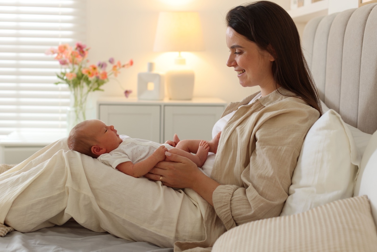 A mother sitting up in bed, smiling at her newborn on her lap