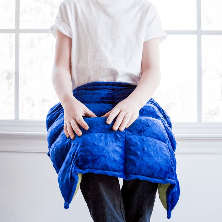 A child seated with a blue Harkla weighted lap pad across the lap
