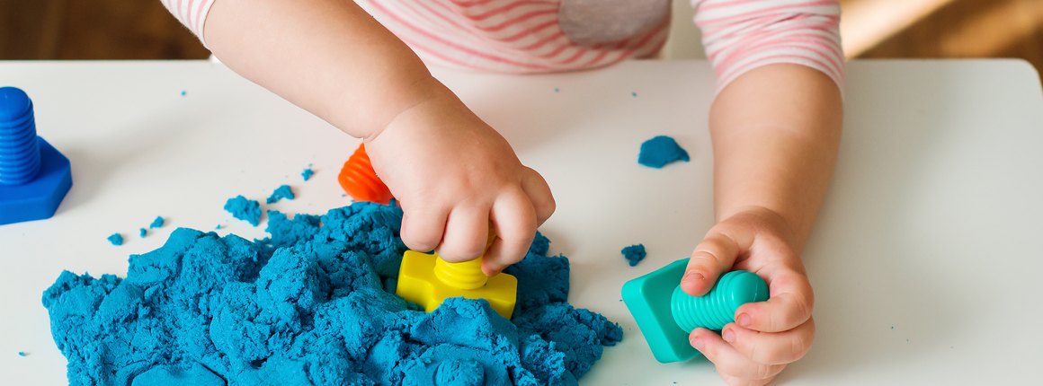 A toddler's hands pressing shapes into blue kinetic sand
