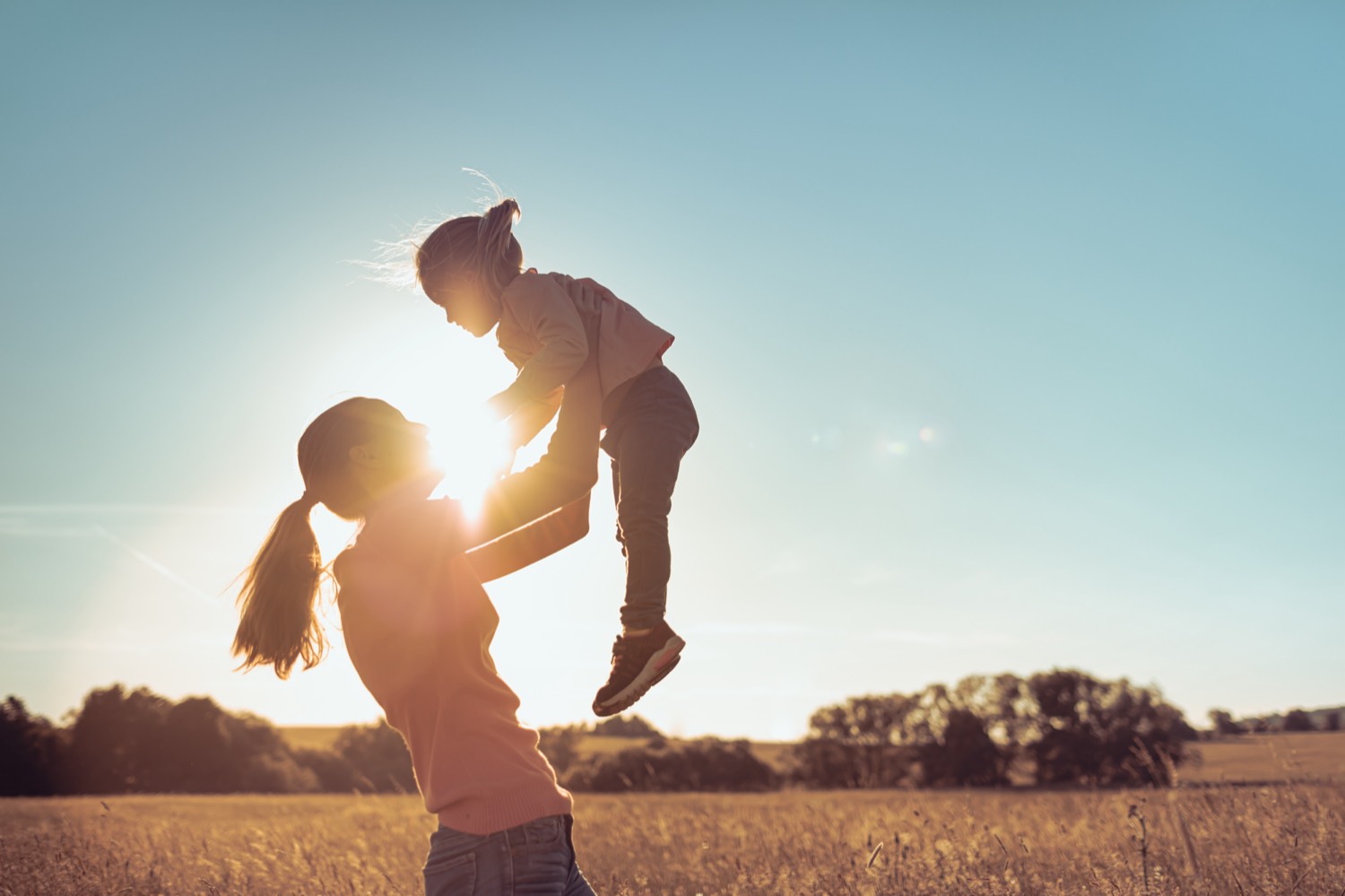 A mother lifting her child into the air in a field at sunset