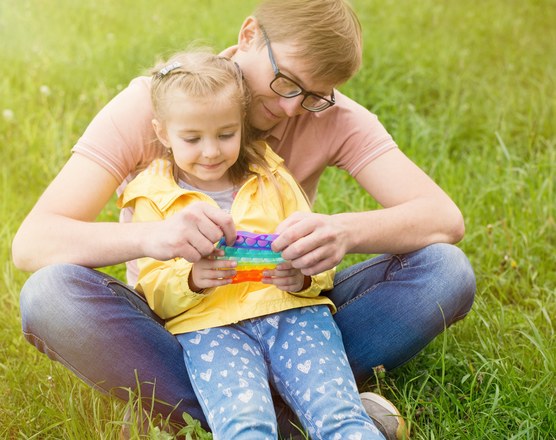 A mother and daughter sitting on the grass playing with a rainbow pop-it
