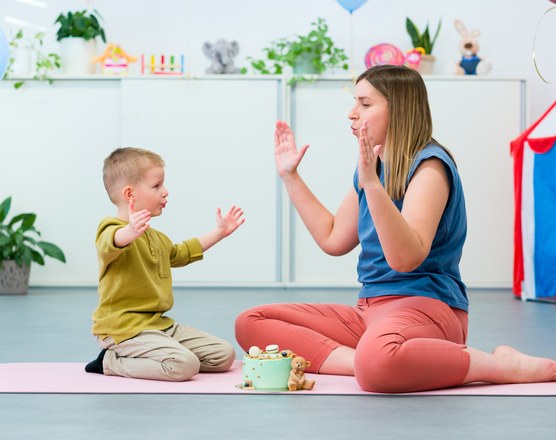 A therapist and a young boy clapping together during a session on a play mat