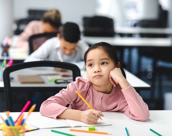 A girl resting her chin on her hand and looking away from unfinished work at a classroom desk