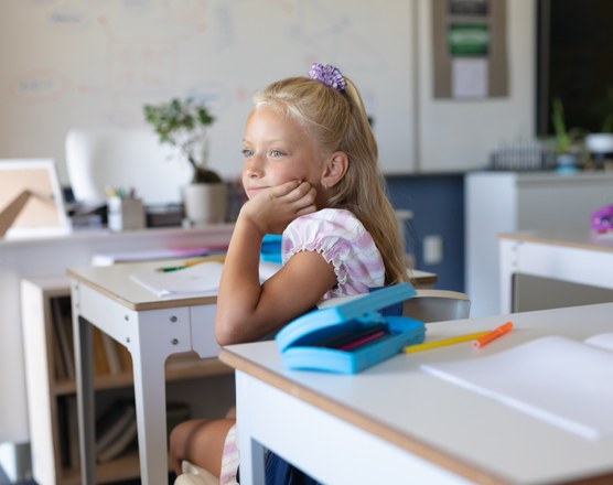 A girl sitting at a classroom desk with her chin on her hand, thinking