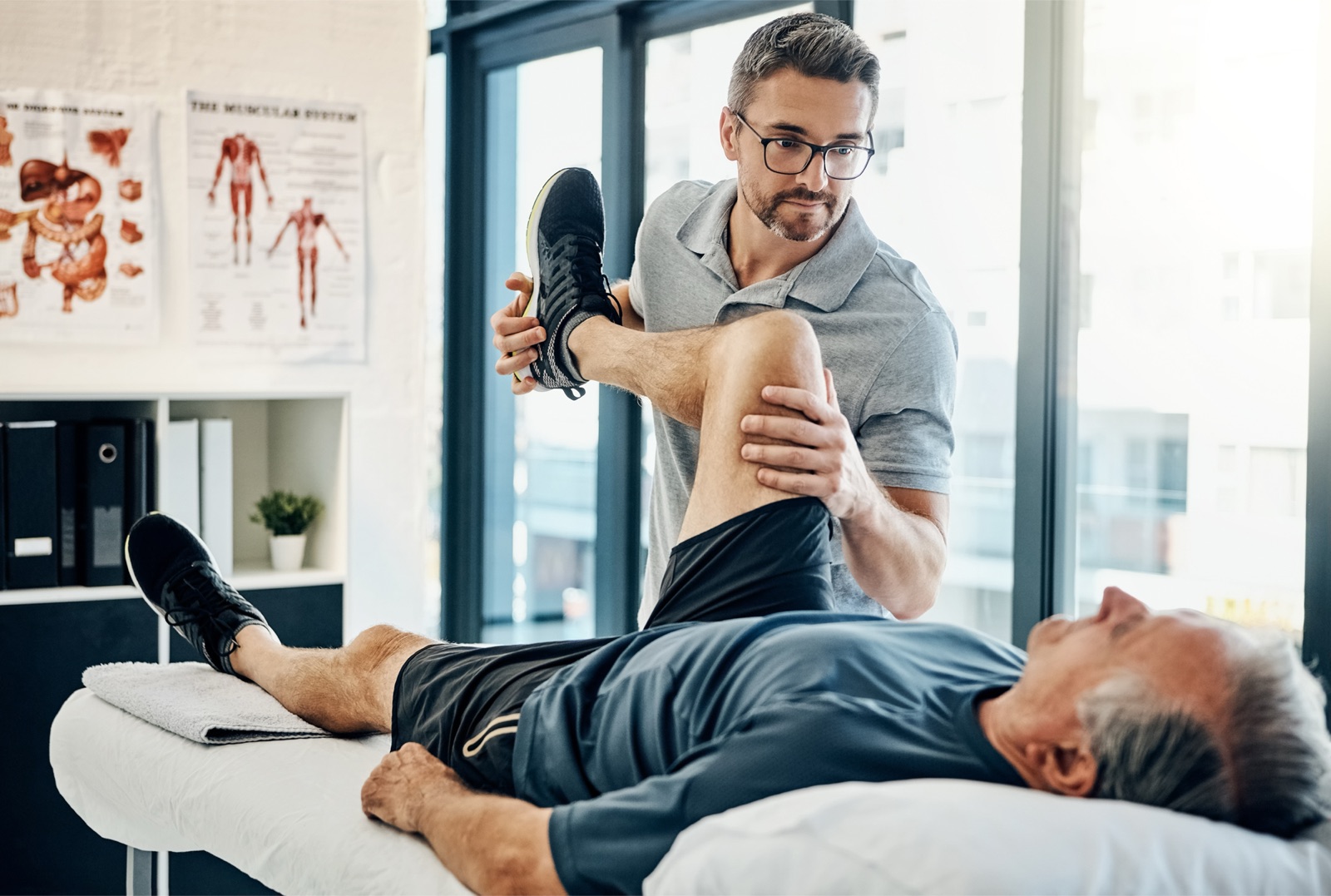 A physical therapist supporting an older adult's leg during a hip and knee assessment on a treatment table.