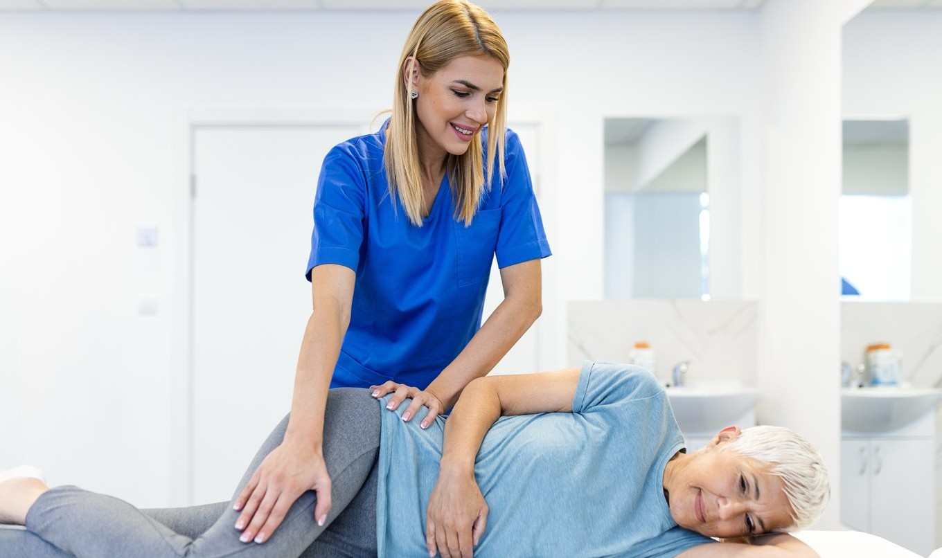 A physical therapist supporting a patient's hip and pelvis during an assessment on a treatment table.