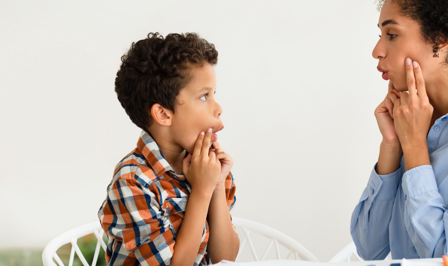 A speech therapist and a boy facing each other, both shaping a sound with their mouths