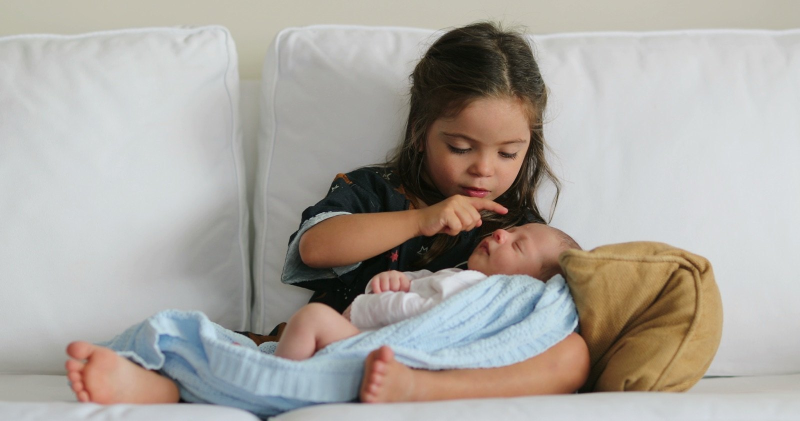 An older sister lying beside her sleeping newborn sibling