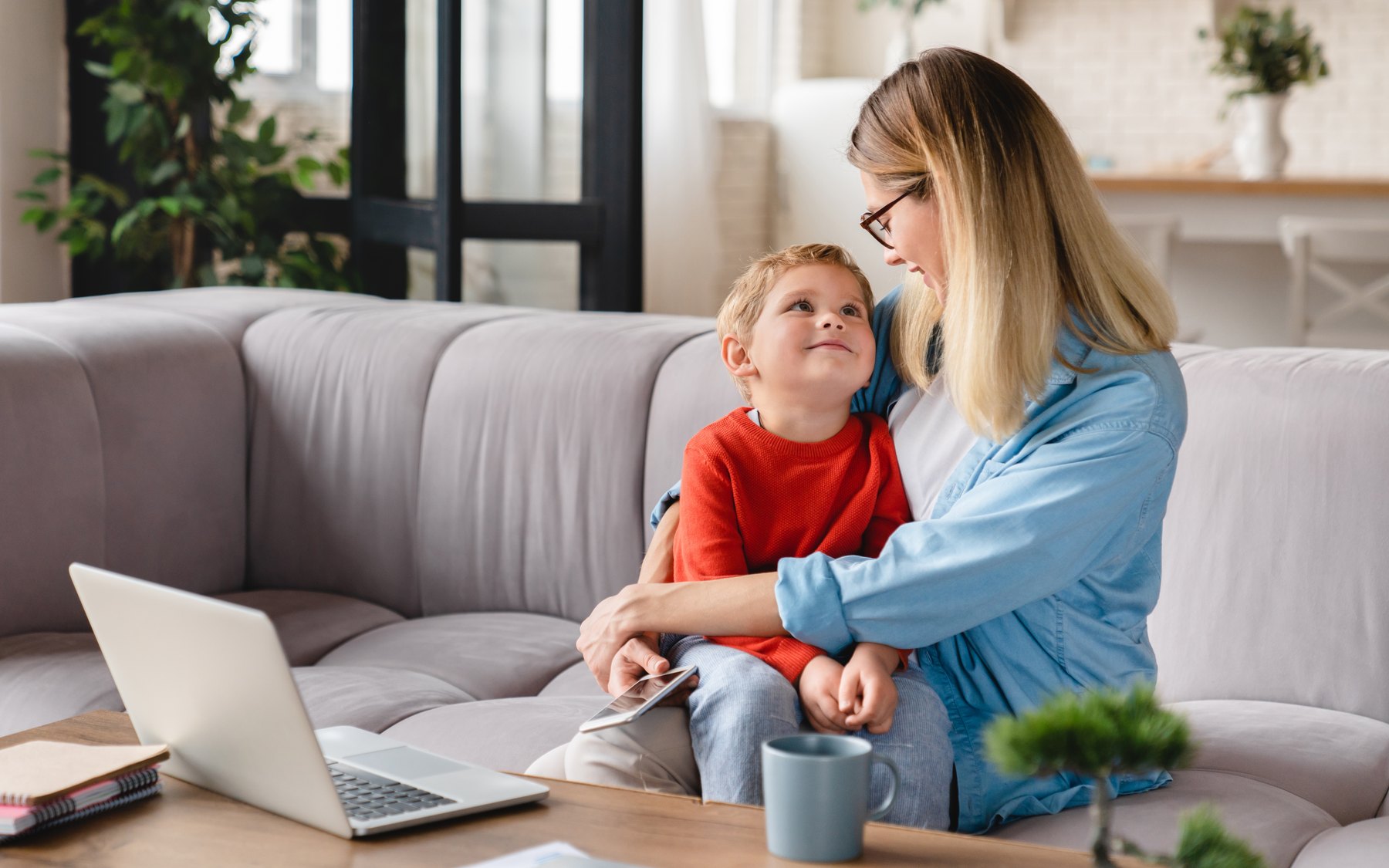 A mother and her school-age son sitting together on a sofa, turned toward each other mid-conversation