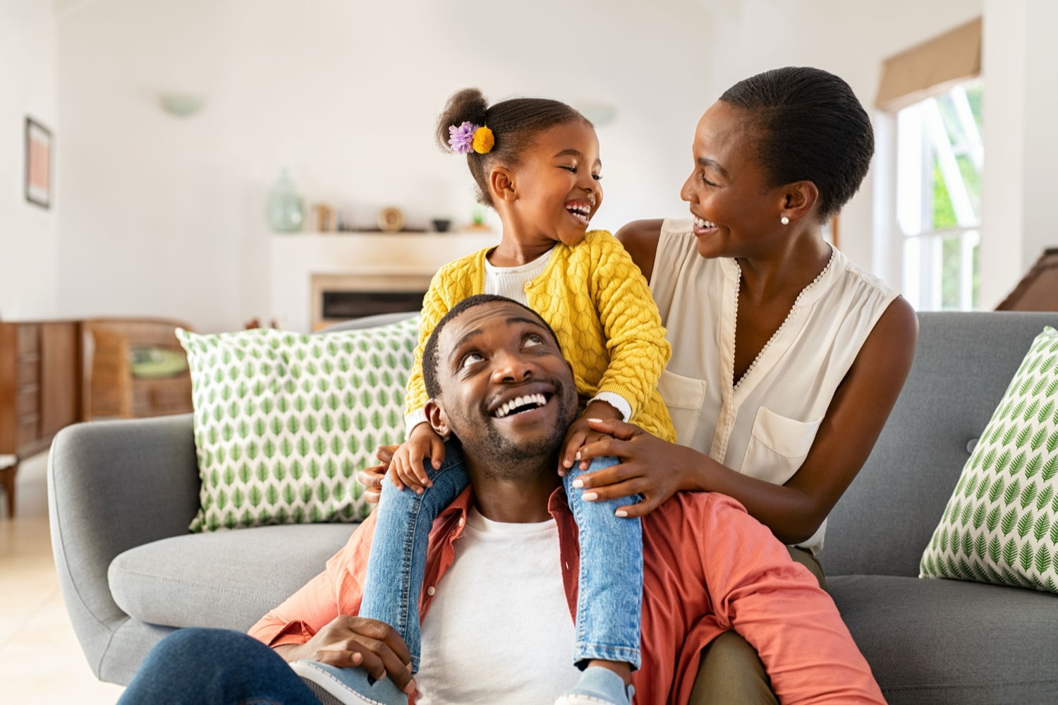 Two parents and their young daughter laughing together on a sofa at home