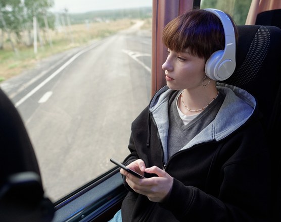 A young person wearing over-ear headphones on a coach, looking out of the window