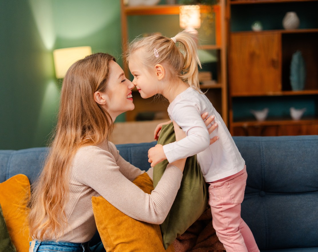 A mother and her young daughter face to face on a sofa
