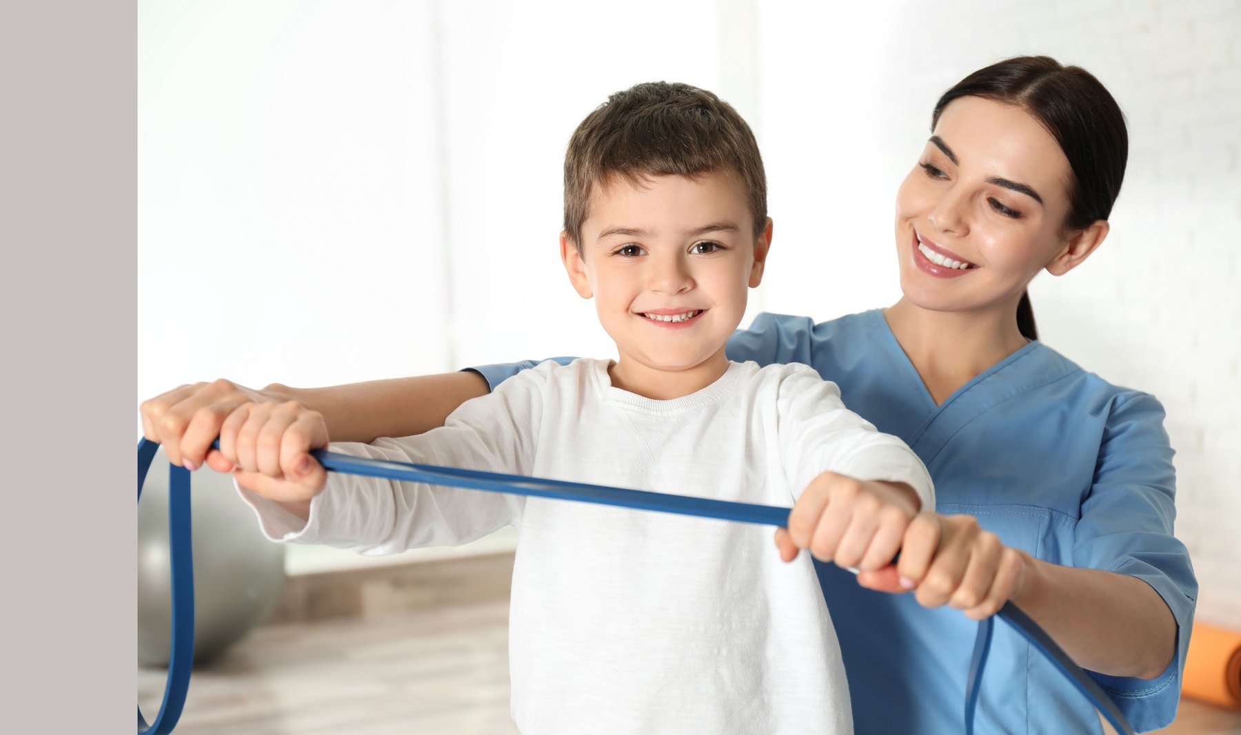 A therapist guiding a boy to stretch a resistance band across his body