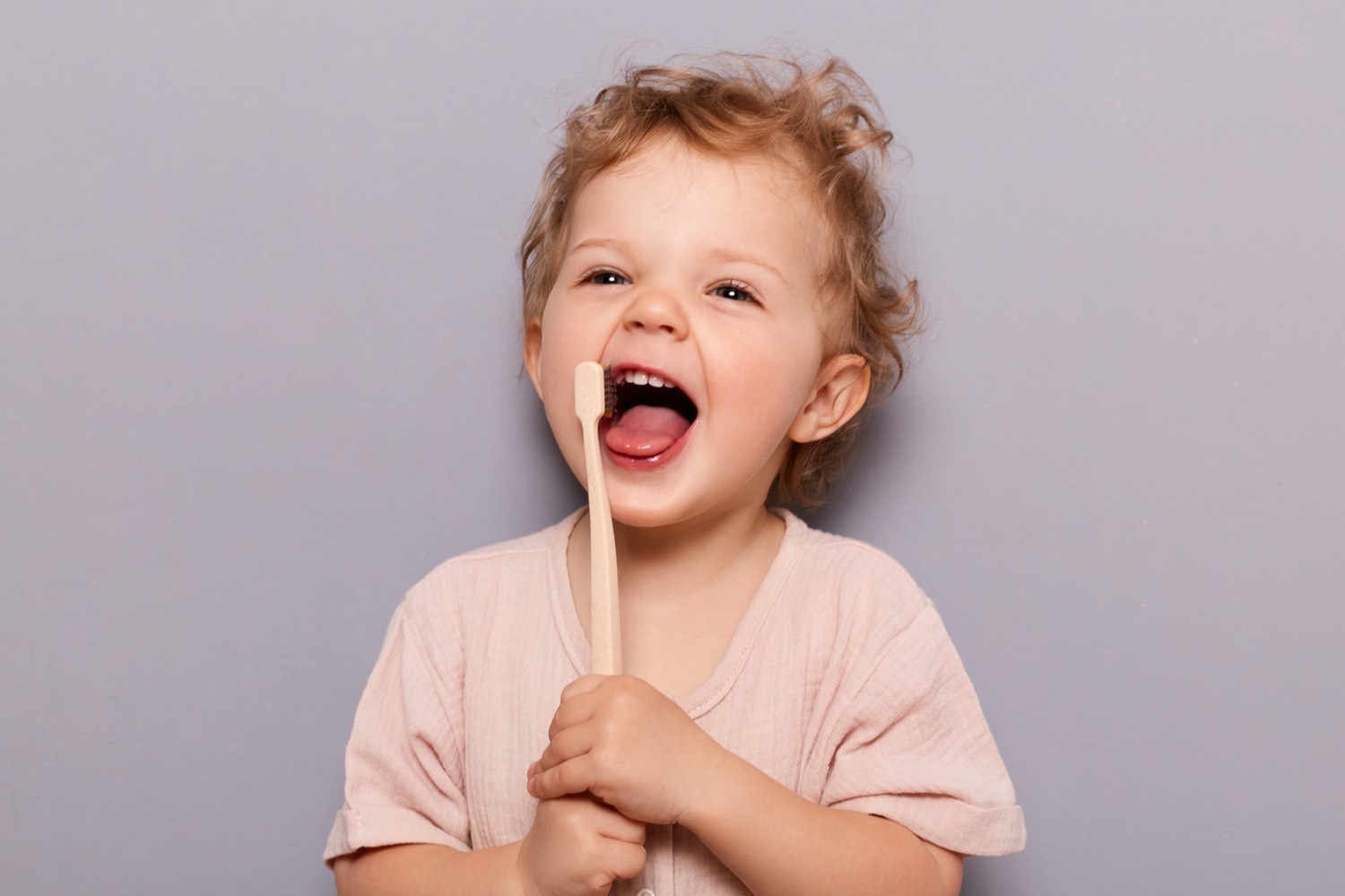 A smiling toddler holding a wooden toothbrush