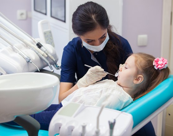 A dentist examining a young girl's teeth in a clinic chair