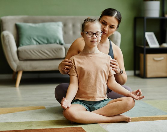 A therapist sitting cross-legged on the floor beside a smiling girl during a session
