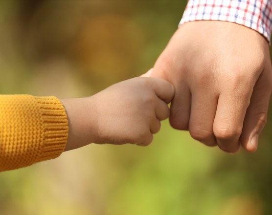 A small child's fist meeting an adult's fist outdoors