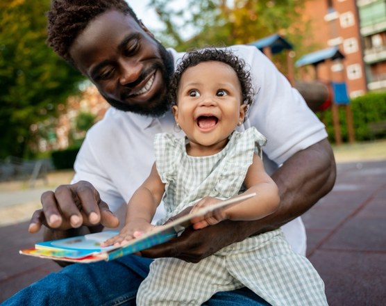 A father sitting outdoors laughing with his baby daughter