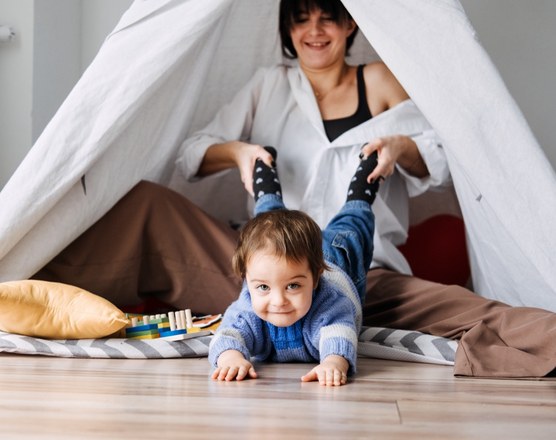A toddler lying on the floor of a blanket fort with a parent behind