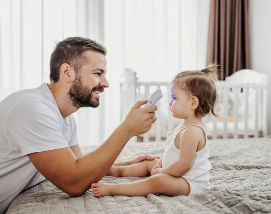 A father holding a digital thermometer to his baby's forehead