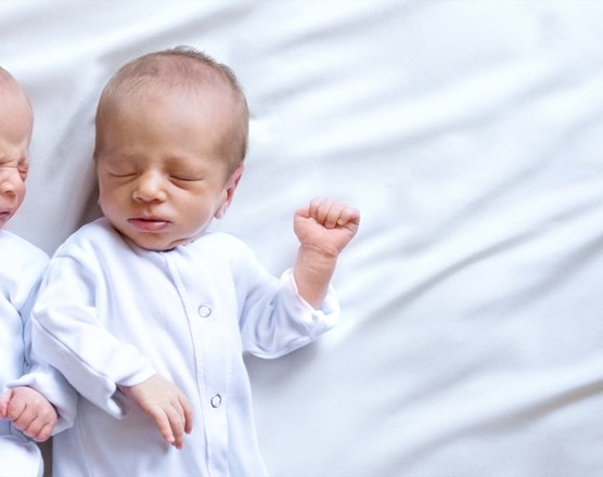 Two newborn twins asleep on their backs on a white sheet
