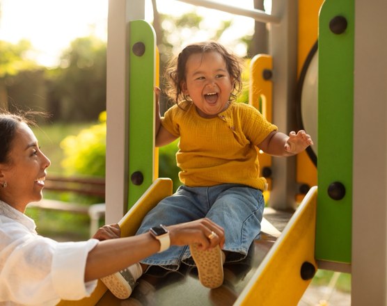 A parent helping a laughing toddler down a playground slide