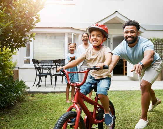 A father running behind a boy learning to ride a bicycle in a garden