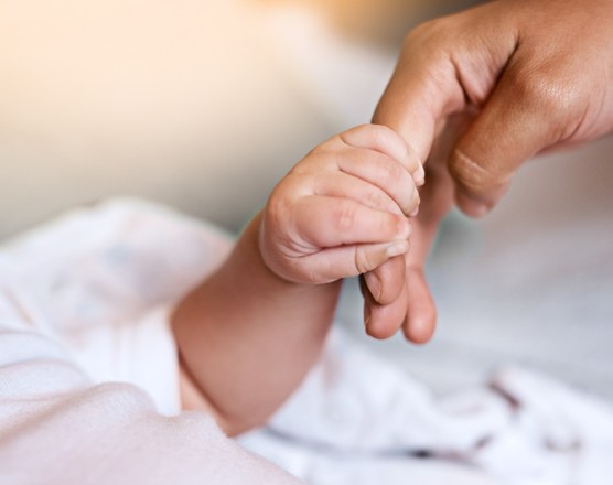 A newborn's hand curled around an adult finger on a white blanket