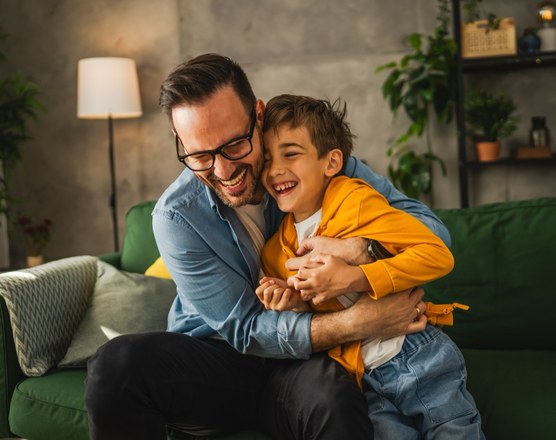 A father sitting on a sofa laughing with his young son