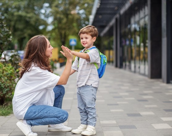 A mother crouching to high-five a small boy wearing a backpack