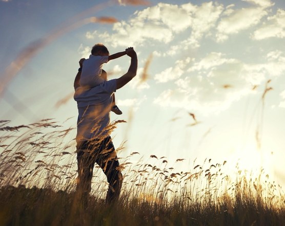 A parent carrying a child on their shoulders through a sunlit field
