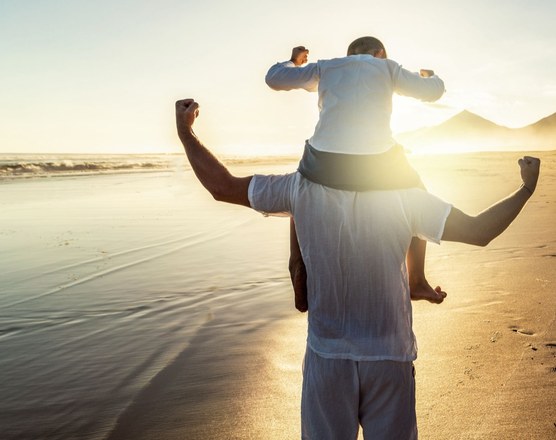 A father carrying a child on his shoulders on a beach at sunset