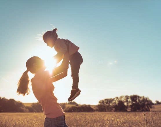 A parent lifting a child into the air in a field at sunset