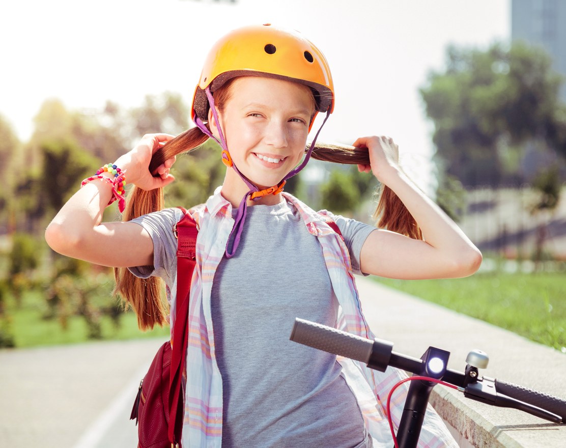 A girl in a helmet standing with her scooter outdoors
