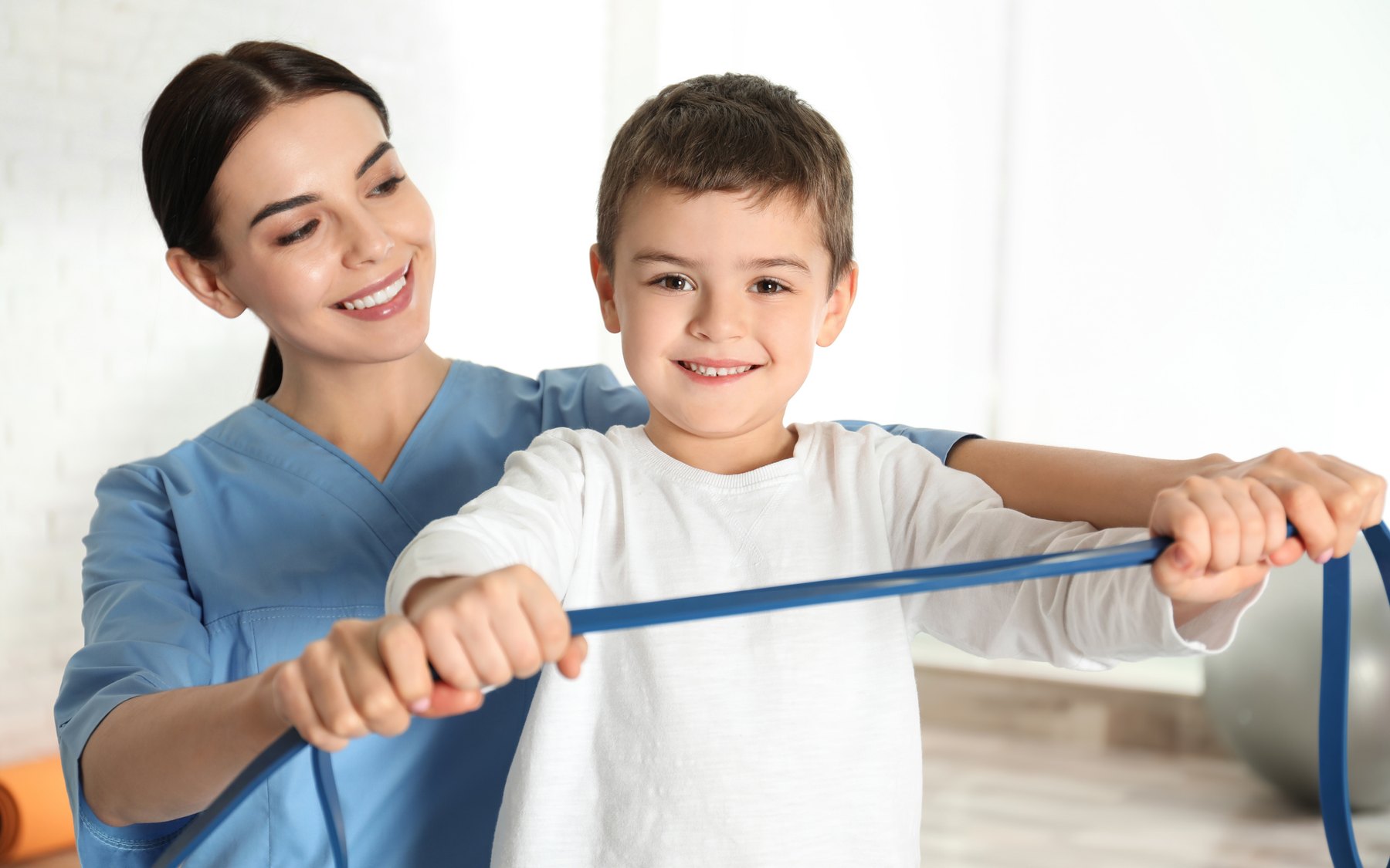 A physical therapist guiding a boy through an exercise with a resistance band