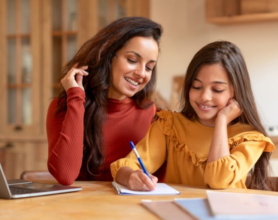 A mother sitting beside her daughter at a laptop, working through homework together