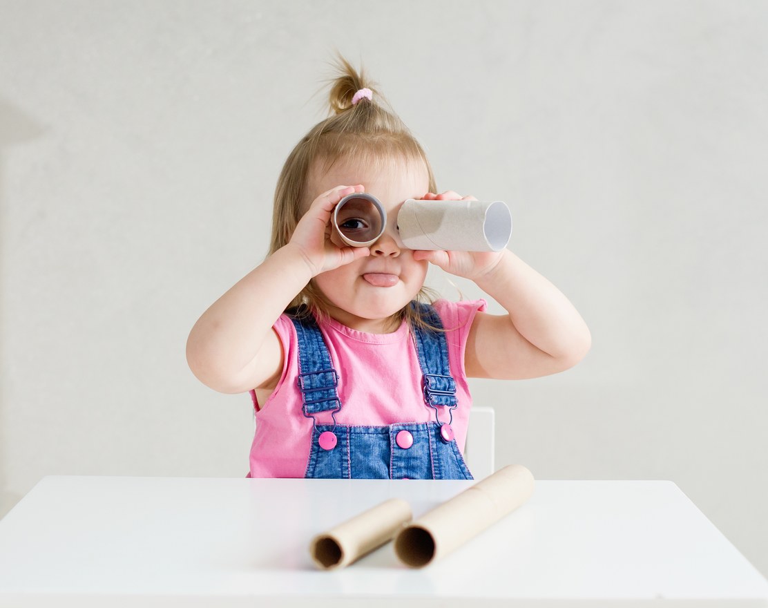 A toddler looking through a cardboard tube