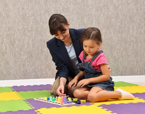 A therapist and a young girl playing with small toys on a foam play mat