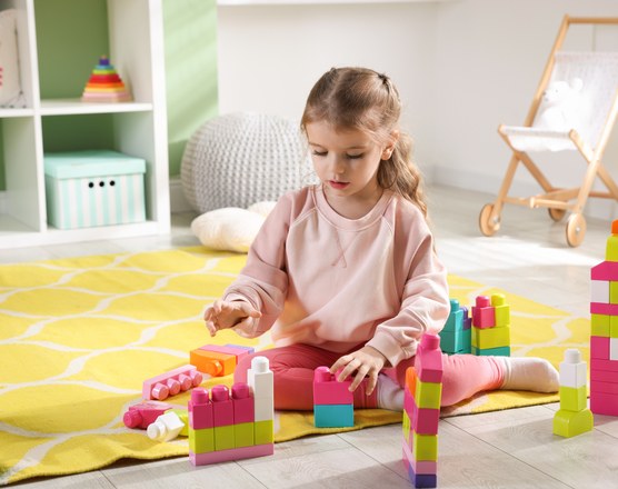 A girl building an elaborate structure from colored blocks on a playroom floor