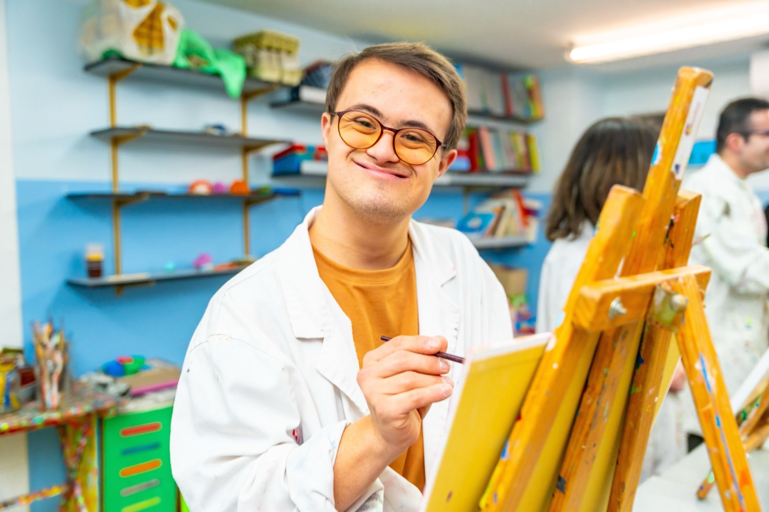 A young adult in an art studio smiling while painting at an easel