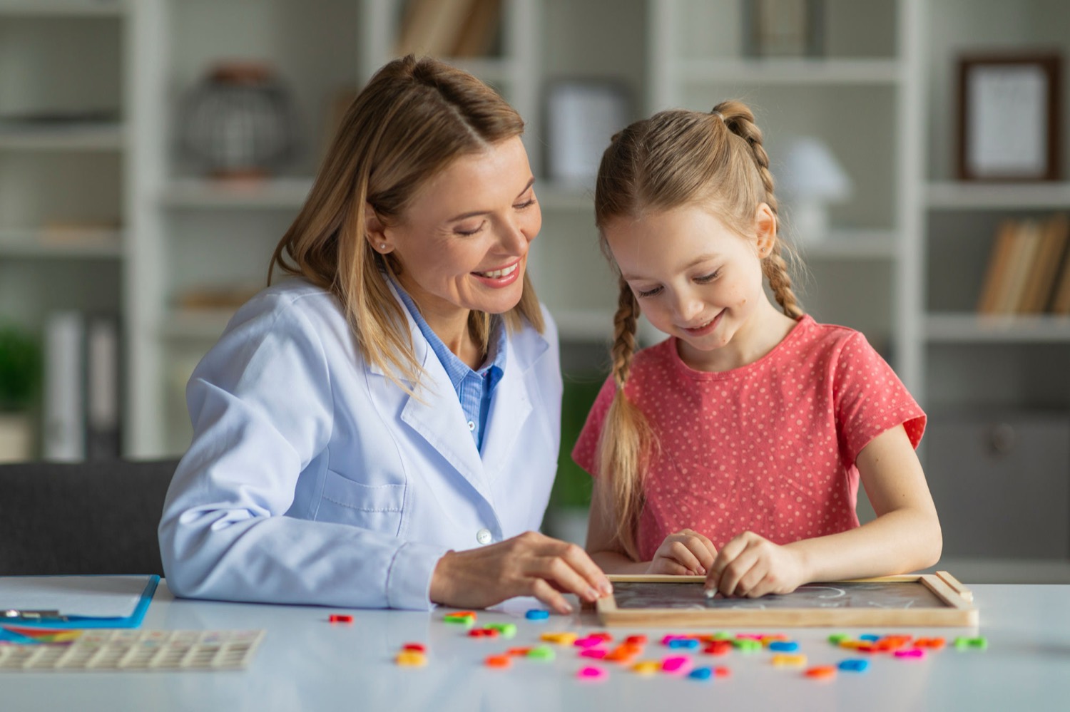 A clinician sitting with a young girl at a table, working with colored letters on a board