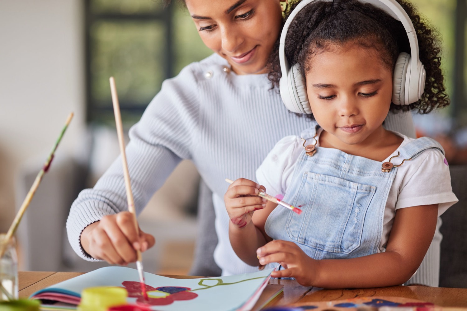A young girl wearing ear defenders painting at a table with her mother