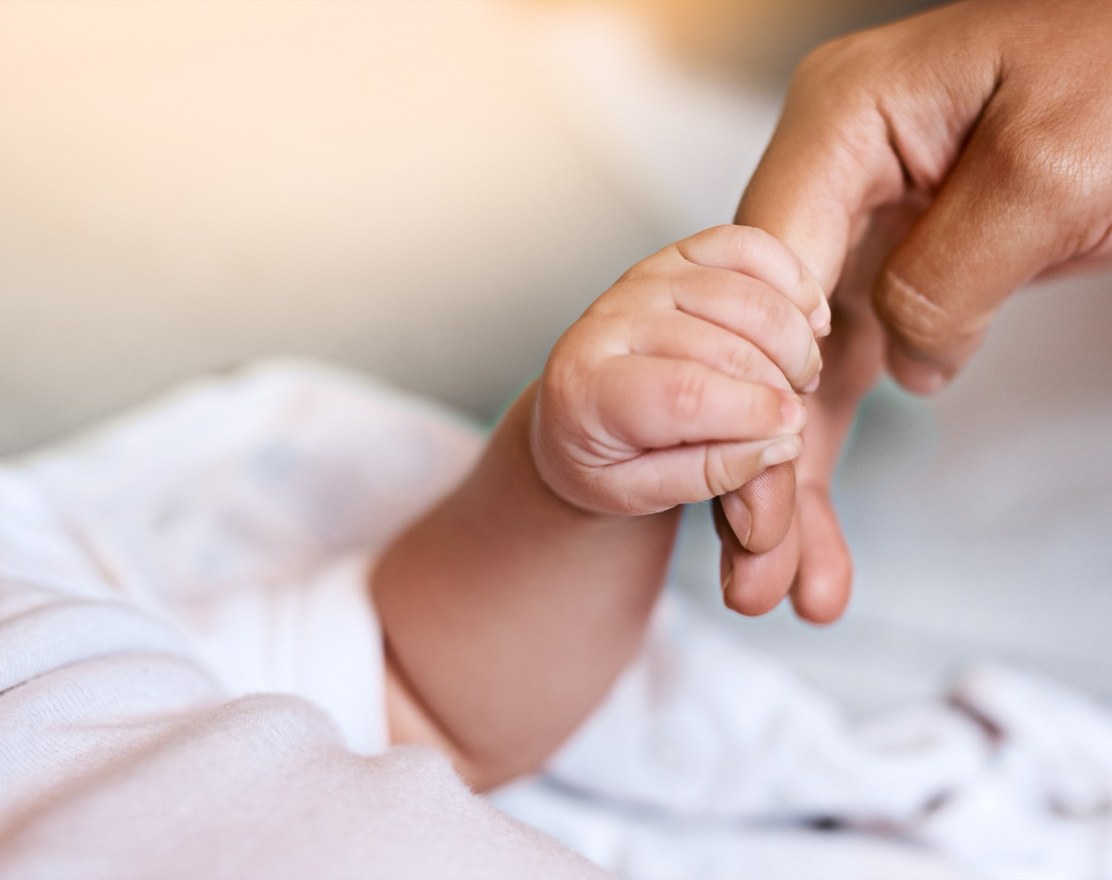 A newborn's hand curled around an adult finger