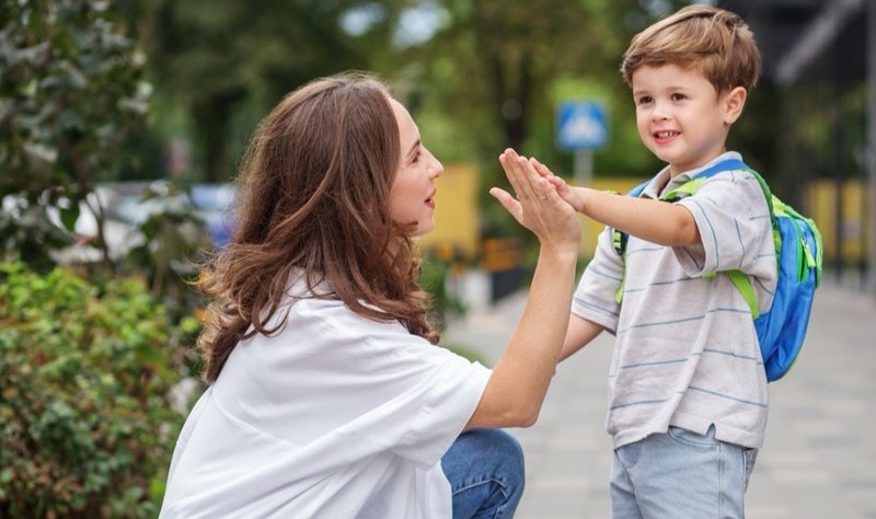 A parent high-fiving a child wearing a school backpack