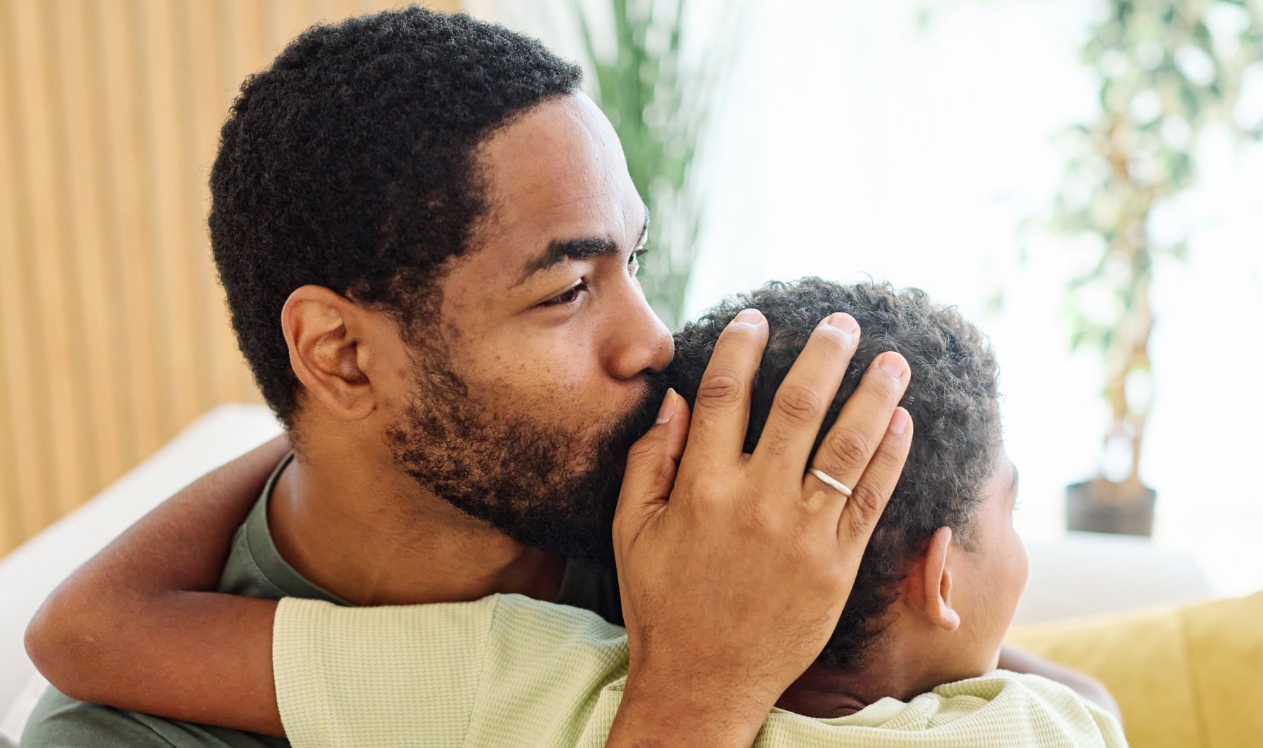 A father holding his young son close, one hand cradling the back of his head