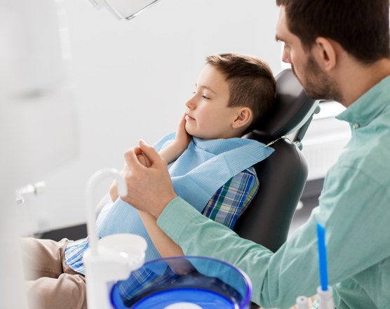 A dentist examining a boy's jaw as he sits back in a dental chair