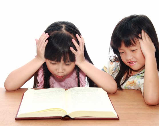 Two girls holding their heads in frustration over an open book